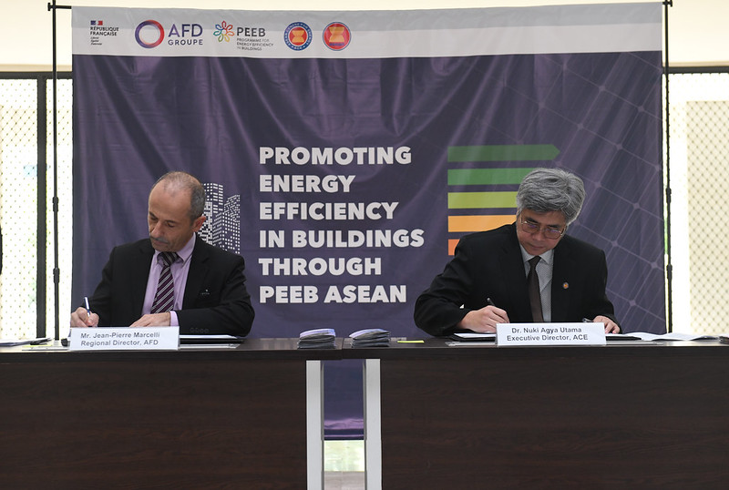 Two men sit at a table signing papers for the PEEB ASEAN grant agreement